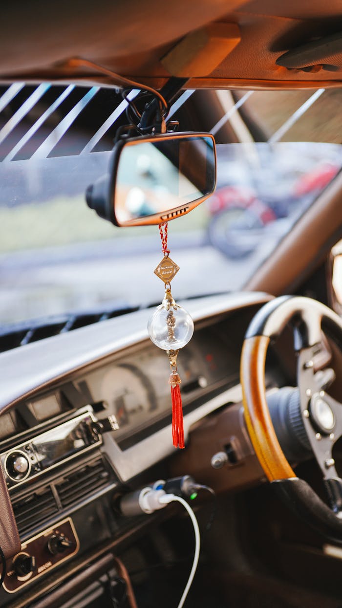 Close-up of a vintage car's dashboard and rear-view mirror with hanging ornament.